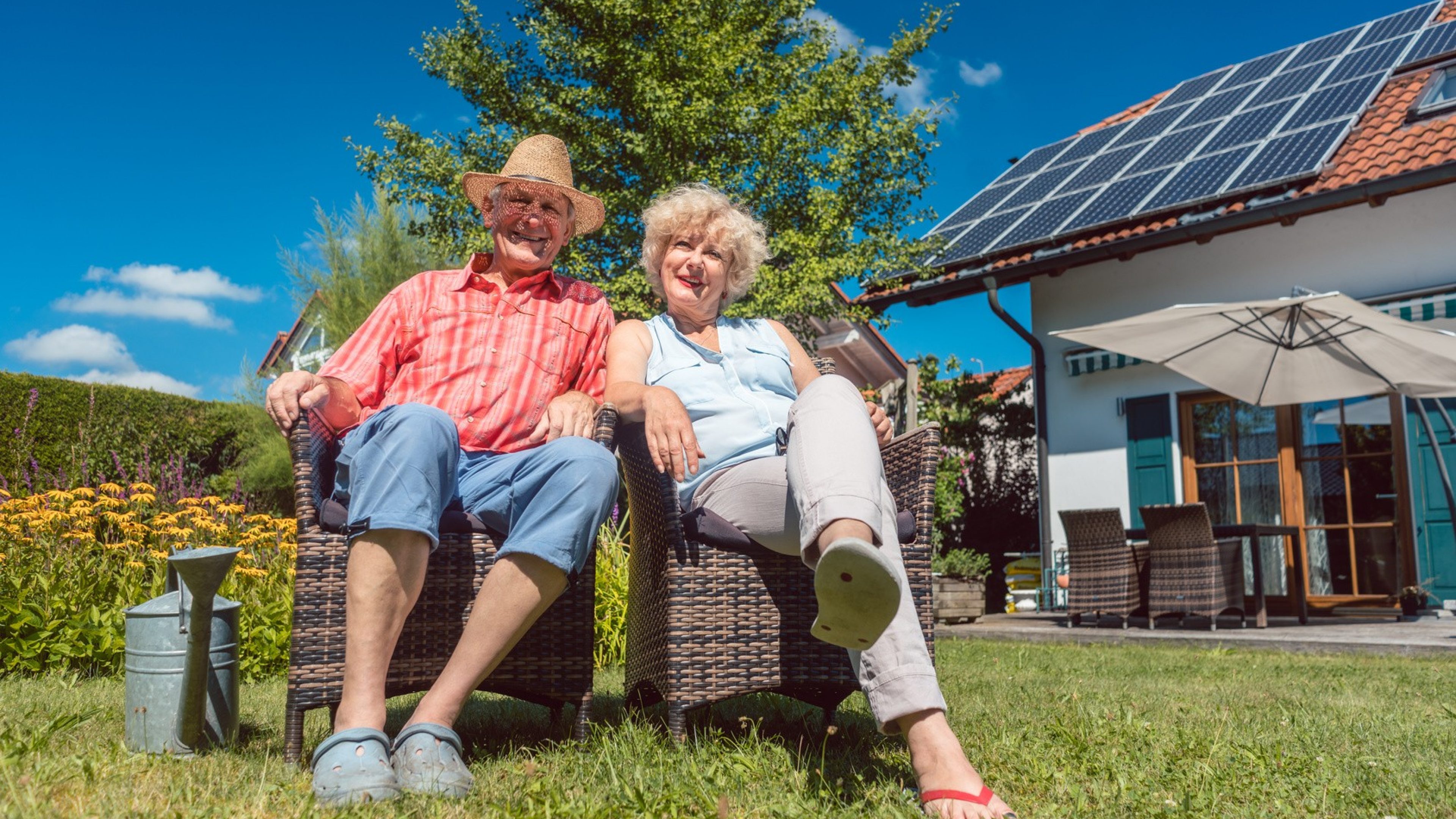 Low-angle view portrait of a happy senior couple in love sitting on chairs while relaxing together in the garden at home in a sunny day of summer