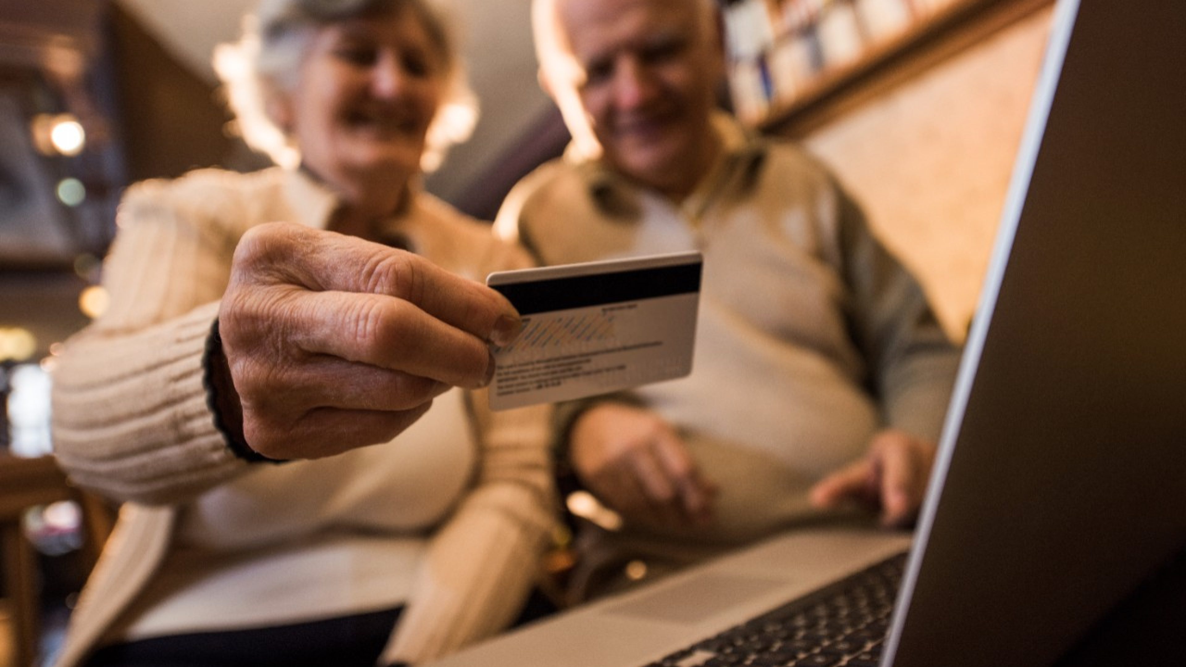 Close up of a senior man holding credit card and shopping with his wife via Internet.